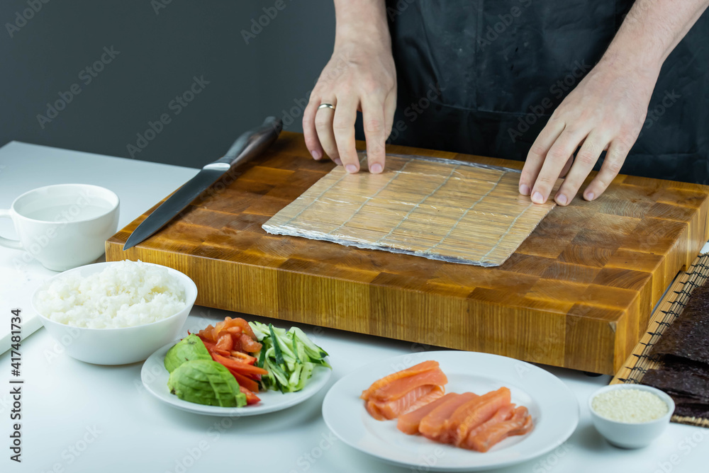 Closeup of chef hands preparing japanese food. Professional chef making sushi at restaurant. Man hands making traditional asian sushi rolls on cutting board. Closeup of chef hands preparing japanese food. Professional chef making sushi at restaurant. Man hands making traditional asian sushi rolls on cutting board.