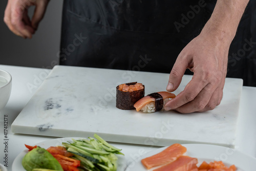 Closeup of chef hands preparing japanese food. Professional chef making sushi at restaurant. Man hands making traditional asian sushi rolls on cutting board.