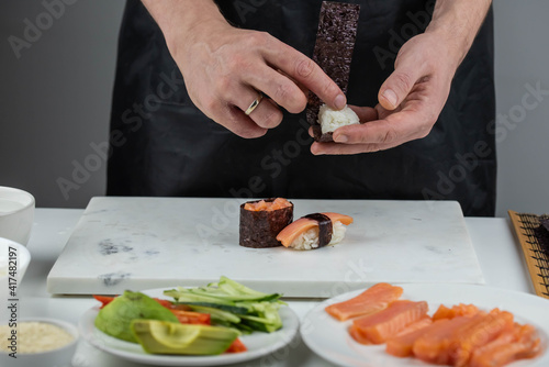 Closeup of chef hands preparing japanese food. Professional chef making sushi at restaurant. Man hands making traditional asian sushi rolls on cutting board.