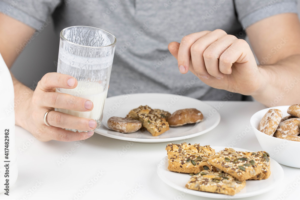 Man having breakfast with milk or kefir and healthy grain cookies on white background. Young man eating healthy food. 