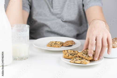 Man having breakfast with milk or kefir and healthy grain cookies on white background. Young man eating healthy food. 