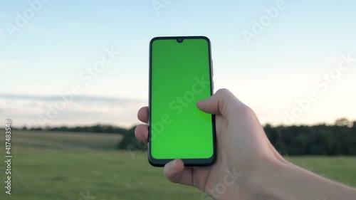 Man holding mobile phone, smartphone on a background of nature, endless fields and forests. Green screen, blank phone, application.Swipe to the right with your thumb