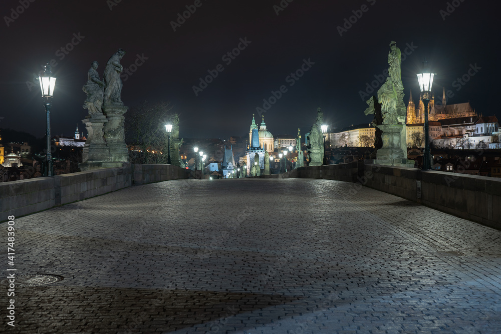 Naklejka premium lit lanterns and illuminated statues and sidewalk with cobblestones on an empty charles bridge at night during a lockdown