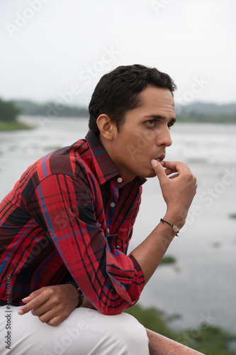 Portrait of a dark-haired man dressed in red looking right on a bridge, thinking about family problems. Mental illness