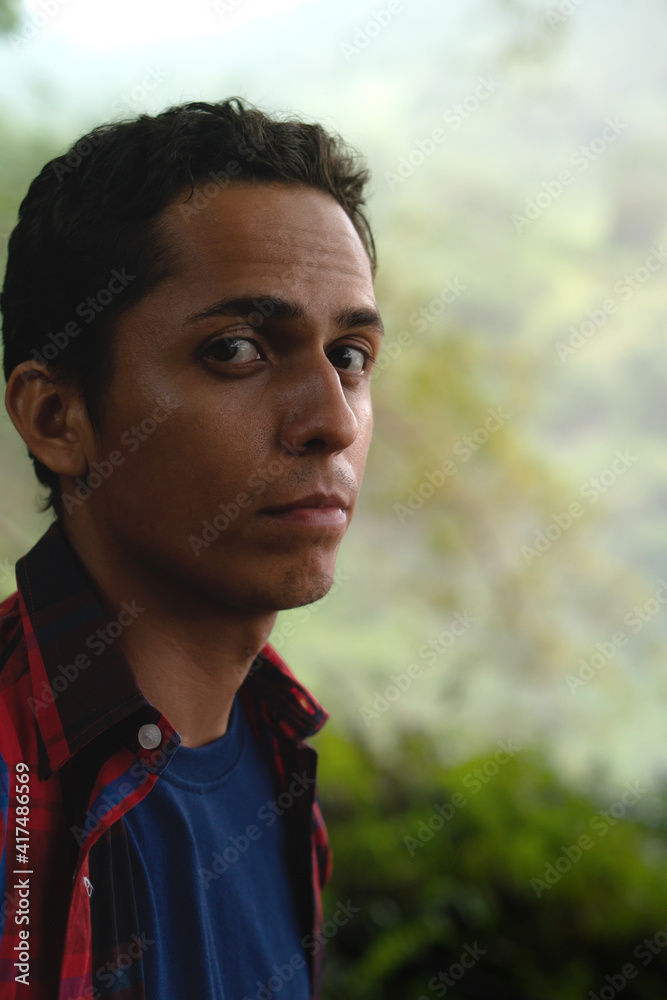Portrait of hispanic man in the middle of a humid forest, dark area within the forest, young man with brown skin dressed in red and blue. Portrait of hispanic man in the middle of a humid forest, dark area within the forest, young man with brown skin dressed in red and blue.