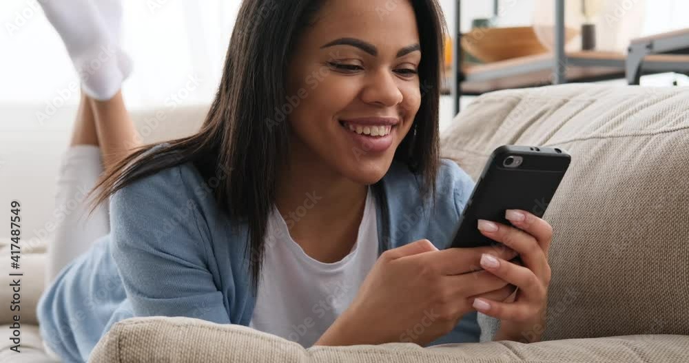 Woman text messaging using mobile phone lying on sofa at home Woman text messaging using mobile phone lying on sofa at home