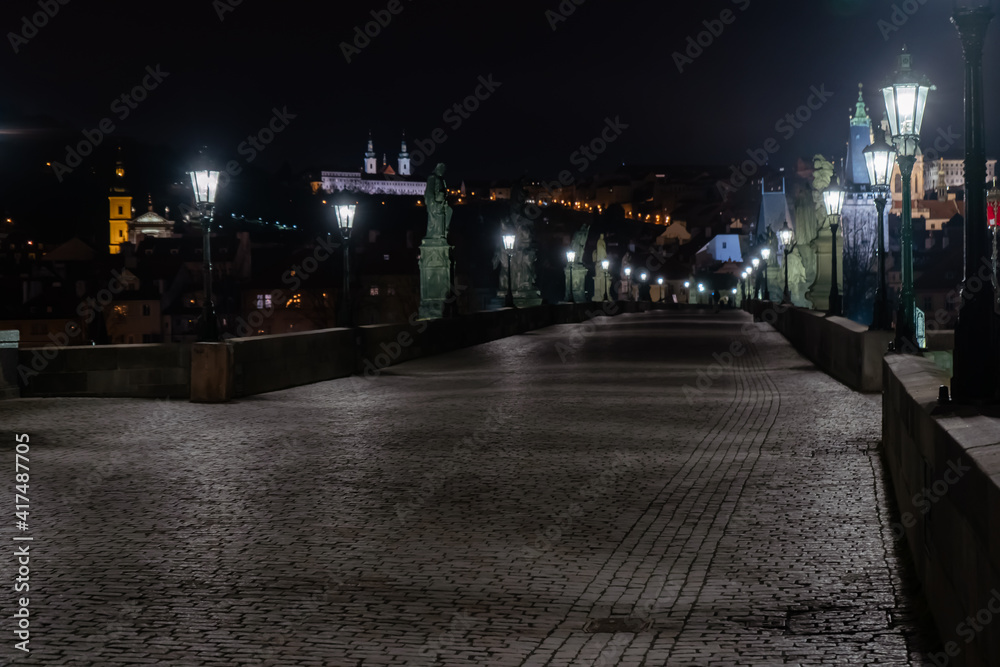 Fototapeta premium view of a stone pavement light from a lantern on an empty charles bridge and an illuminated statue