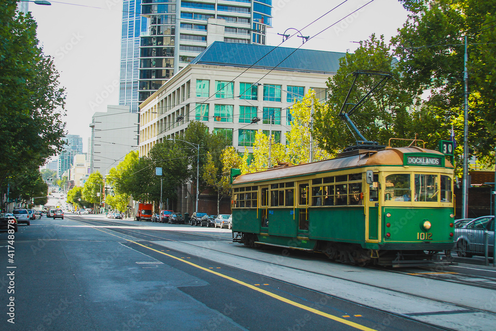 Vintage tram in Melbourne, Australia, rolling down the track in a modern district on a sunny day.