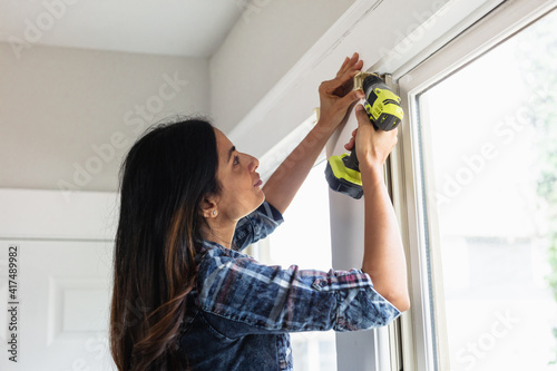 Indian woman using drill power tool to install blinds, DIY home improvement project photo