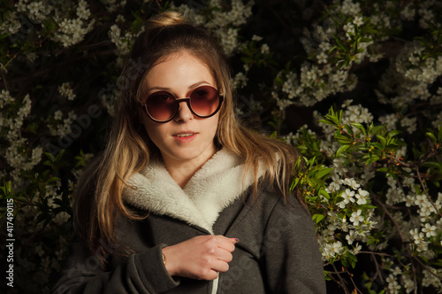 beautiful girl on the street in spring against the background of greenery and flowers in a jacket and sunglasses