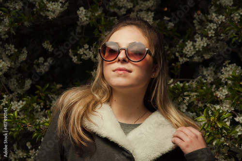 beautiful girl on the street in spring against the background of greenery and flowers in a jacket and sunglasses