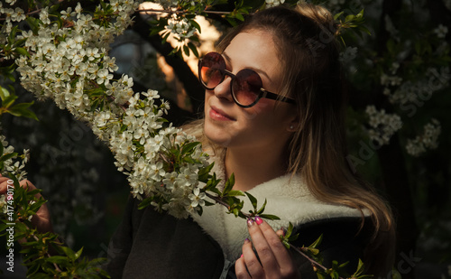 beautiful girl on the street in spring against the background of greenery and flowers in a jacket and sunglasses