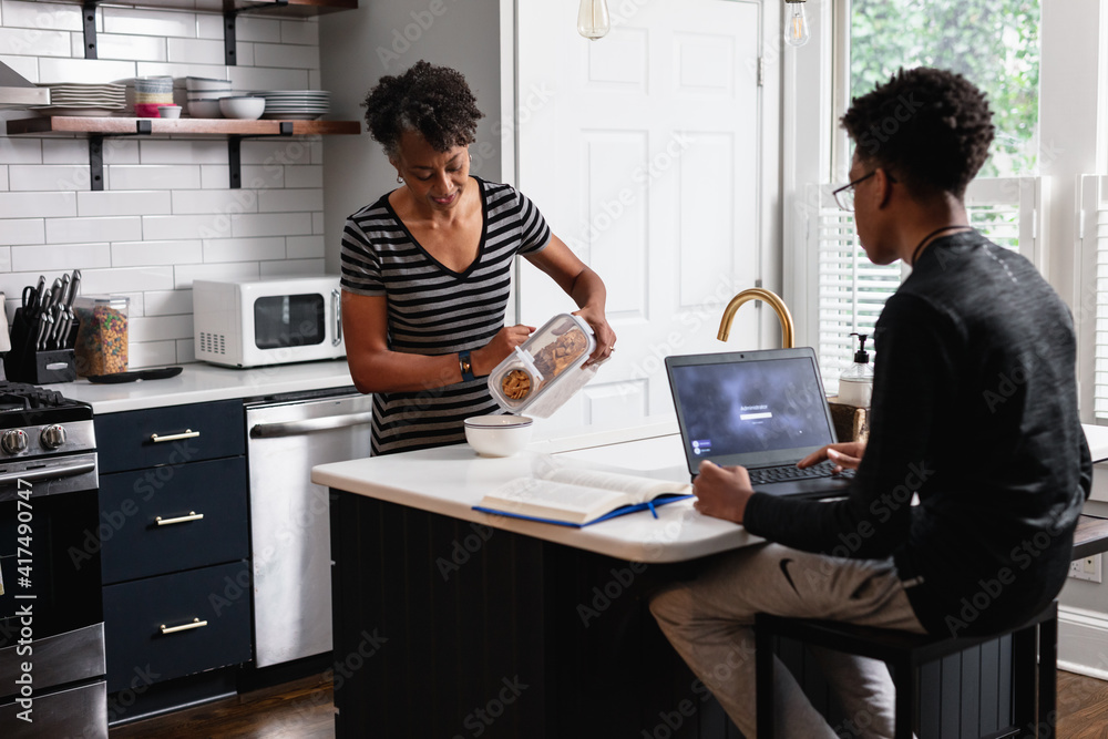 Black mother preparing breakfast cereal for son studying on laptop Black mother preparing breakfast cereal for son studying on laptop
