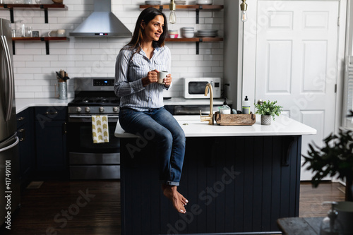 Young Indian woman sitting on kitchen counter, with tea drink photo