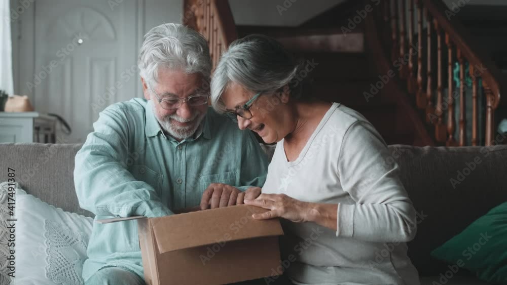 Happy mature aged older family couple unpacking carton box, satisfied with internet store purchase or unexpected gift, feeling excited of fast delivery shipping service, positive shopping experience.
