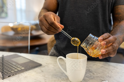 Black man adds honey sweetener to tea drink photo