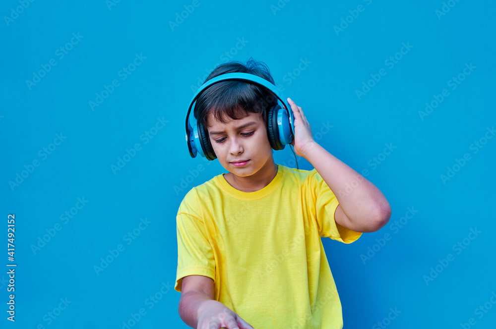 Portrait of smiling boy in yellow t-shirt and blue headphones playing DJ, on blue background. Copy space Portrait of smiling boy in yellow t-shirt and blue headphones playing DJ, on blue background. Copy space