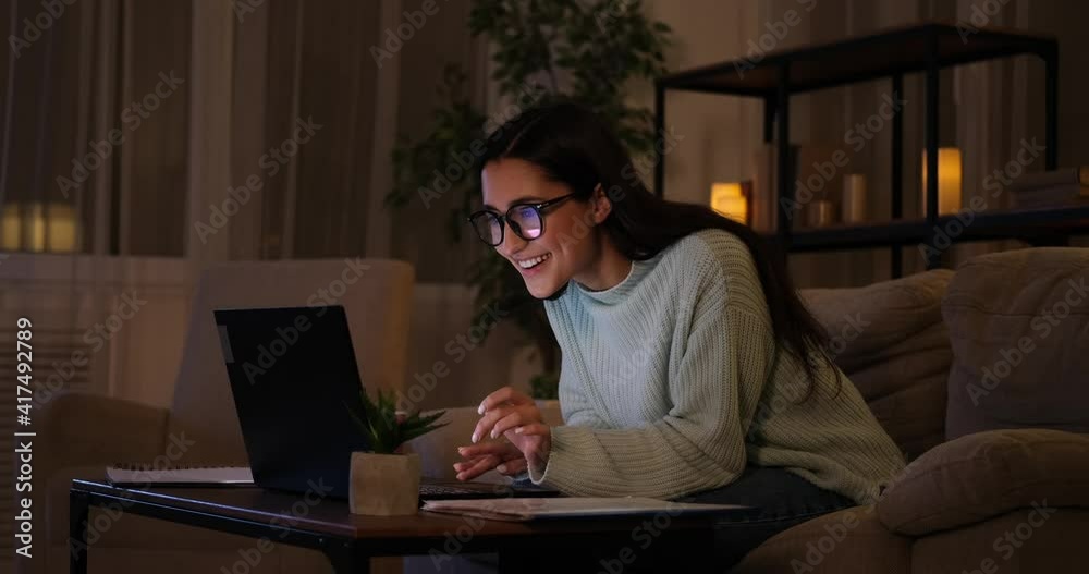 Woman celebrating online success using laptop late night at home Woman celebrating online success using laptop late night at home