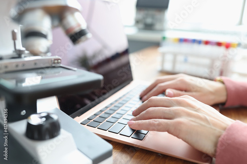 Female hands are working on laptop next to microscope