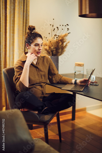 Pregnant woman sitting at home and using laptop.