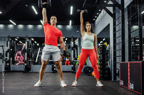 The fitness team does arm exercises with weights in the gym with a black base. With strong movements. They lift heavy weights over their heads. Couple goal, sports lifestyle