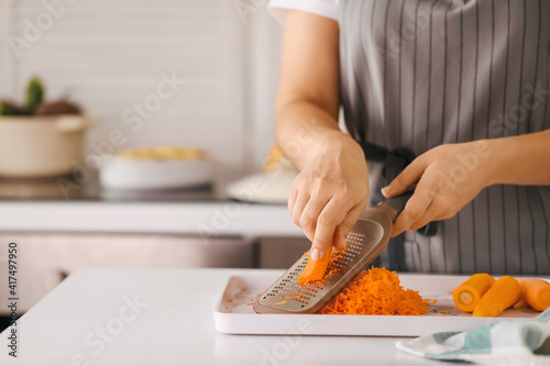 Woman grating carrot in kitchen