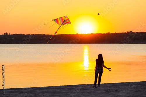 Woman flying kite near river at sunset