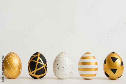 Canvas Print Easter golden decorated eggs stand in a row on white background