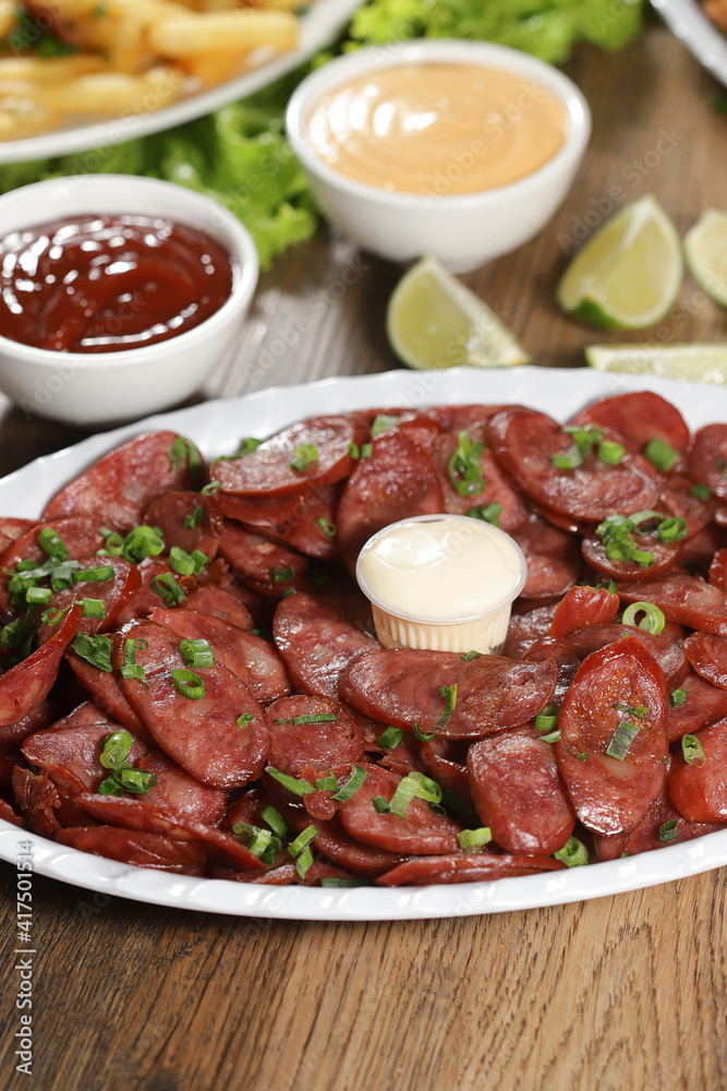 Portion of pepperoni sausage with lemon. Lettuce, green onion, ketchup and mayonnaise