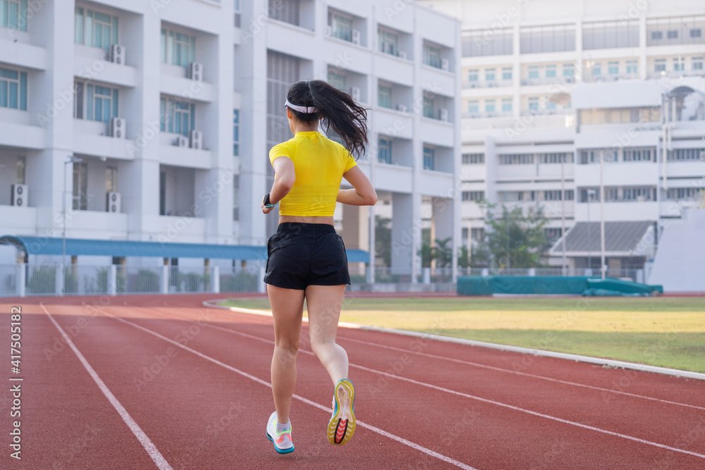 A young Asian woman athlete runner jogging on running track in city stadium in the sunny morning to keep fitness and healthy lifestyle. Young fitness woman runs on stadium track. Sport and recreation A young Asian woman athlete runner jogging on running track in city stadium in the sunny morning to keep fitness and healthy lifestyle. Young fitness woman runs on stadium track. Sport and recreation