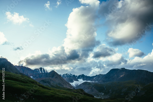 Dramatic alpine landscape with mountain ridge under cloudy sky. Large cloud in blue sky above silhouettes of mountain range. Big cloud in gradient sky above mountains silhouettes and beautiful glacier