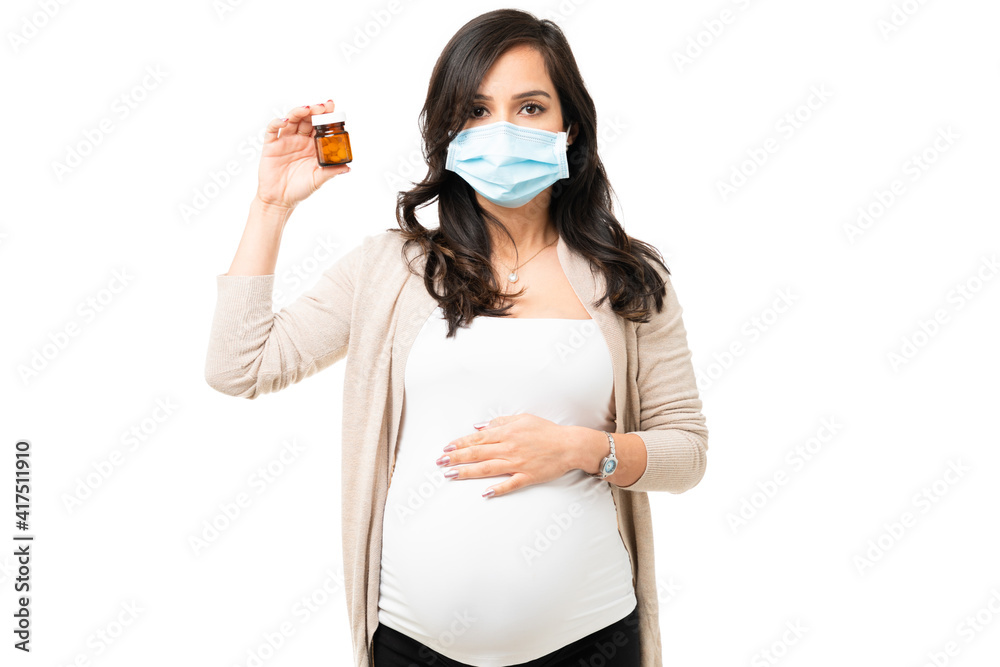 Caucasian pregnant woman with a face mask and a bottle of pills