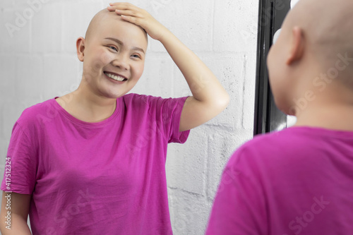 Young adult female cancer patient looking in the mirror, smiling.