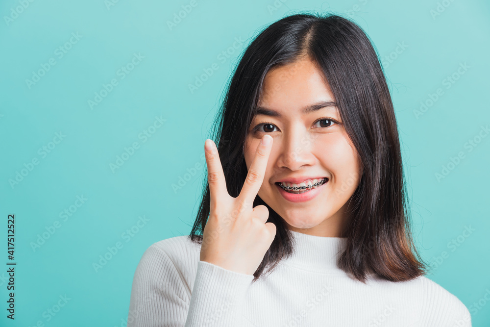 Portrait female give V-sign near-eye make Hollywood white smile, Young beautiful Asian woman showing peace gesture victory, studio shot isolated on a blue background Portrait female give V-sign near-eye make Hollywood white smile, Young beautiful Asian woman showing peace gesture victory, studio shot isolated on a blue background
