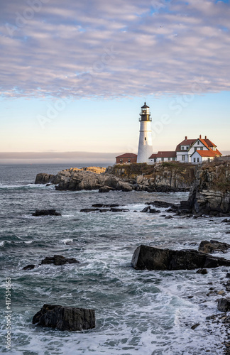 An active lighthouse with ancillary buildings on the rocky coast of the Atlantic Ocean in Maine