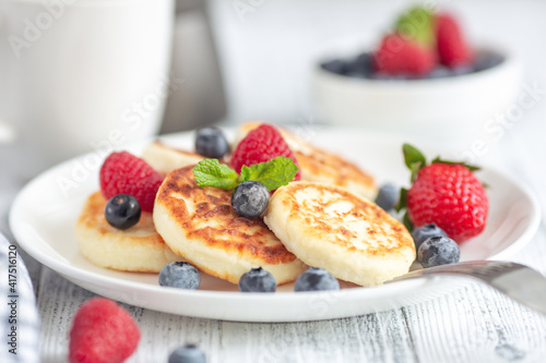 Close up of cottage cheese pancakes with fresh berries on white wooden table. Curd fritters with berries  syrniki. Soft focus - Image