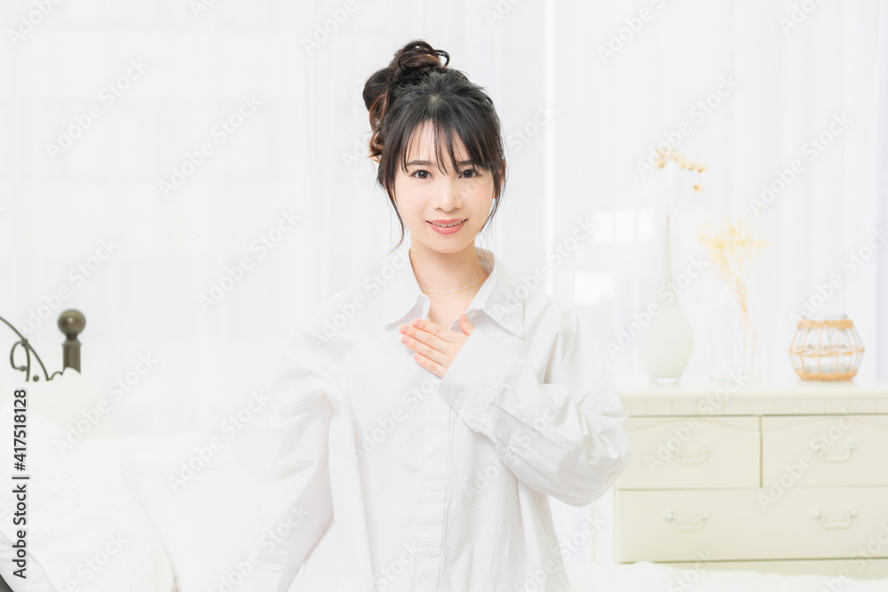 部屋で胸に手を当てる白いシャツを着た若い女性