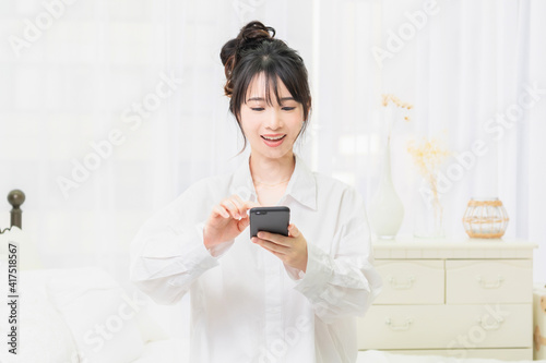 部屋でスマホを使う白いシャツを着た若い女性 © garage38