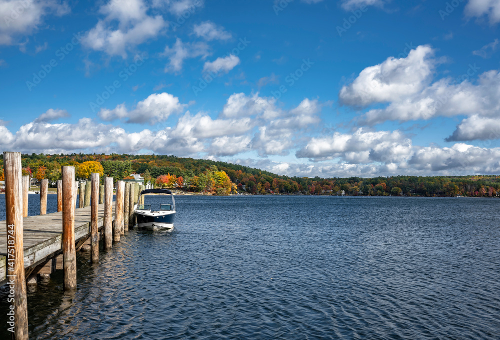 Pleasure motor boat is moored at a wooden pier on a picturesque lake with autumn trees in the hills in Maine
