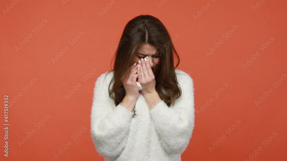 Deeply upset depressed woman in fluffy white sweater crying, desperately wiping tears with napkin, see no way from hopeless situation, break-up, loss. Indoor studio shot isolated on orange background Deeply upset depressed woman in fluffy white sweater crying, desperately wiping tears with napkin, see no way from hopeless situation, break-up, loss. Indoor studio shot isolated on orange background
