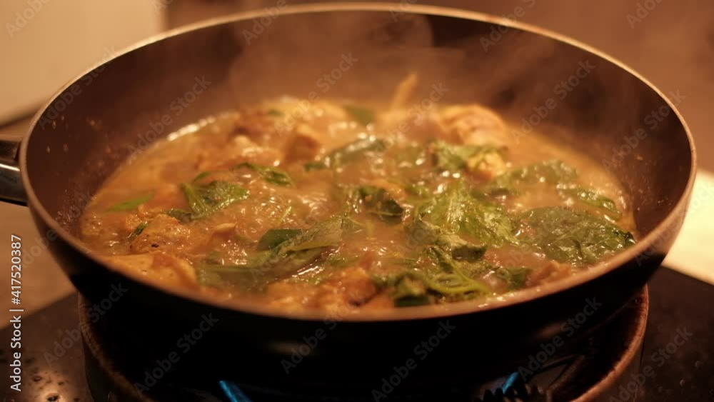 Chicken curry paste is being cooked in a pan over heat from an electric stove. 
