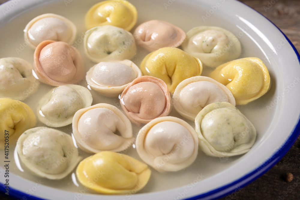 Traditional Russian dumplings made from multi-colored dough in broth. Dumplings on a wooden board in an enamel plate. Cooking concept. Traditional Russian dumplings made from multi-colored dough in broth. Dumplings on a wooden board in an enamel plate. Cooking concept.
