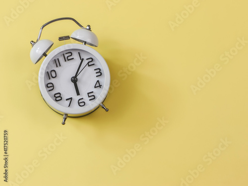 flat lay of white vintage alarm clock on yellow background with copy space.