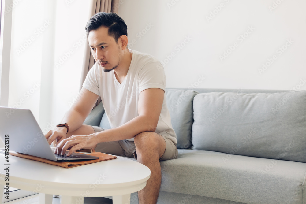 Asian man is working on his laptop in the living room with a cup of coffee. Asian man is working on his laptop in the living room with a cup of coffee.