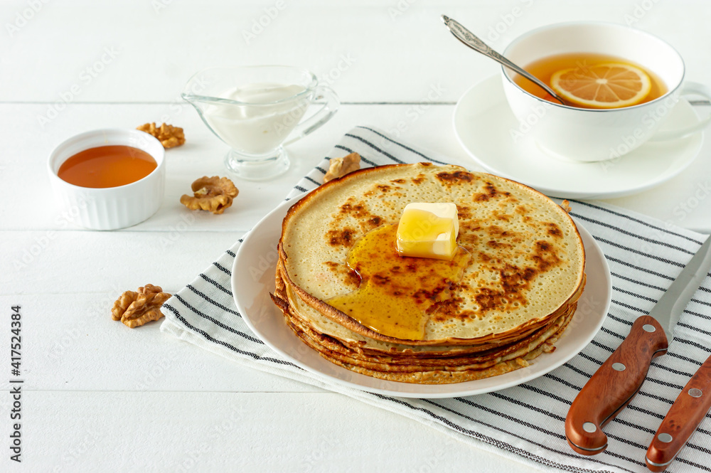Pancakes served with honey syrup and butter on a white plate. Traditional crepes for pancake week or Shrovetide. Pancakes served with honey syrup and butter on a white plate. Traditional crepes for pancake week or Shrovetide.