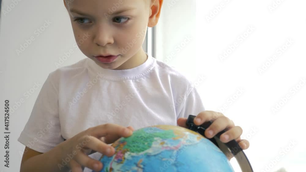 A curious boy sits at the window and studies the continents of the globe. Hobby of children at home, education of preschoolers. A curious boy sits at the window and studies the continents of the globe. Hobby of children at home, education of preschoolers.