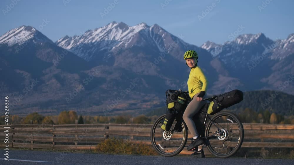 The woman travel on mixed terrain cycle touring with bikepacking. The traveler journey with bicycle bags. Sport tourism bikepacking, bike, sportswear in green black colors. Mountain snow capped. The woman travel on mixed terrain cycle touring with bikepacking. The traveler journey with bicycle bags. Sport tourism bikepacking, bike, sportswear in green black colors. Mountain snow capped.