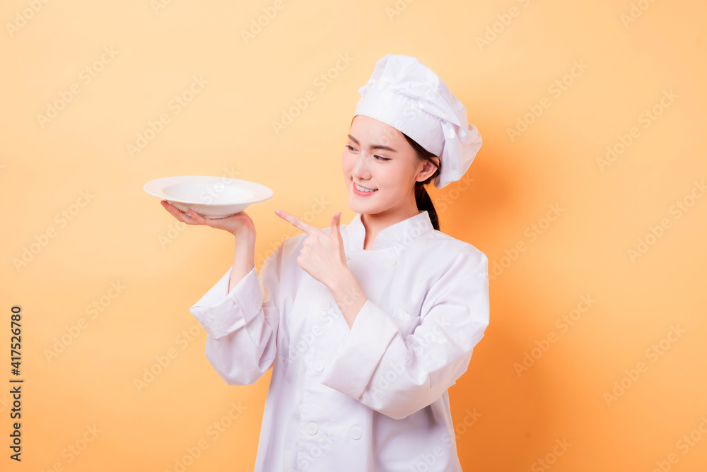 Chef showing empty plate. Happy smiling portrait of female in chef uniform and chef hat isolated on yellow background. Asian woman model. Chef showing empty plate. Happy smiling portrait of female in chef uniform and chef hat isolated on yellow background. Asian woman model.