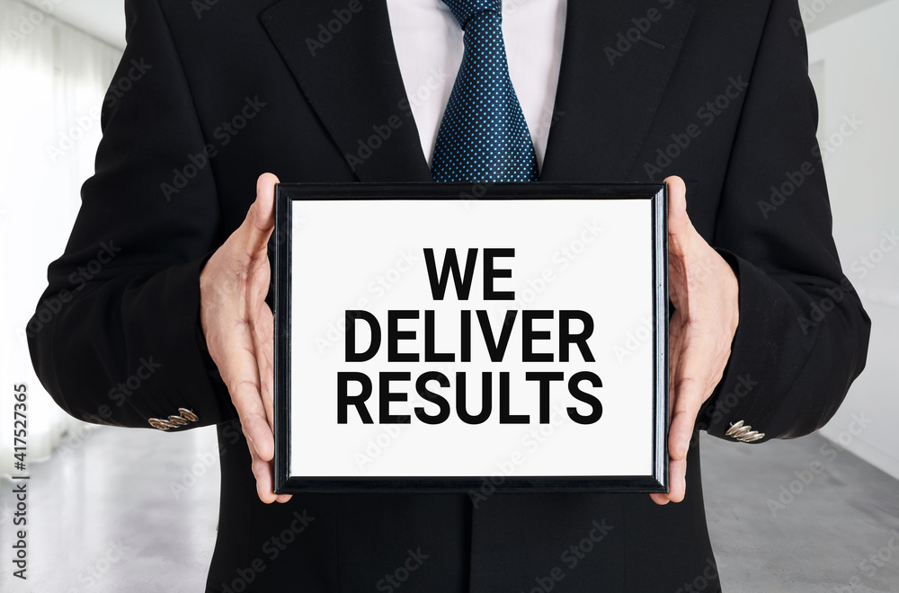 Businessman holds a signboard with the message we deliver results. Businessman holds a signboard with the message we deliver results.