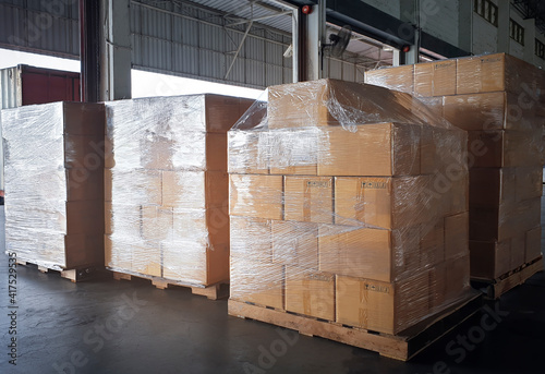 Foto Stacked of cardboard boxes wrapped plastic on pallet rack